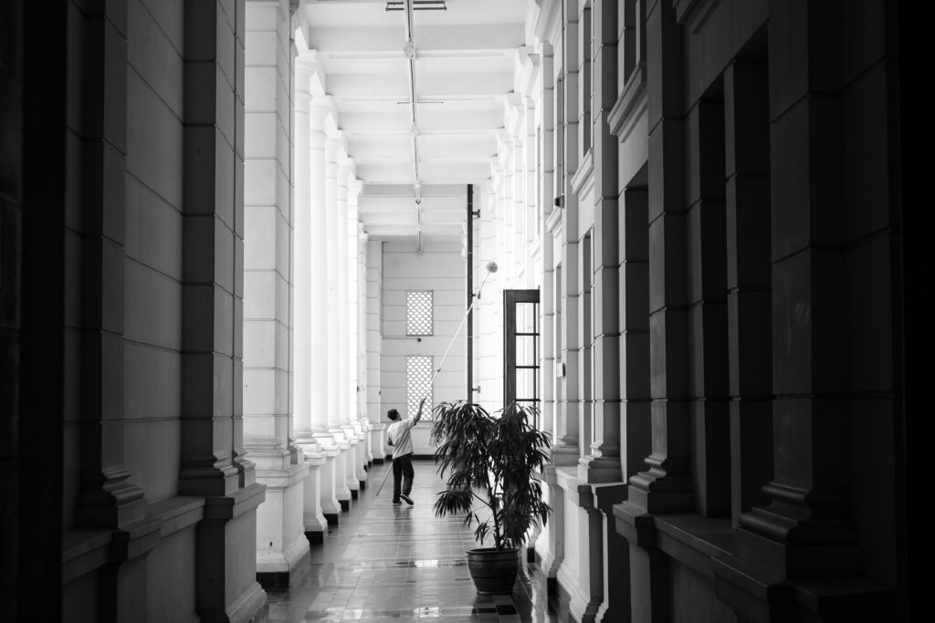 Black and white photo of a man in a hallway with tall columns, conveying elegance.