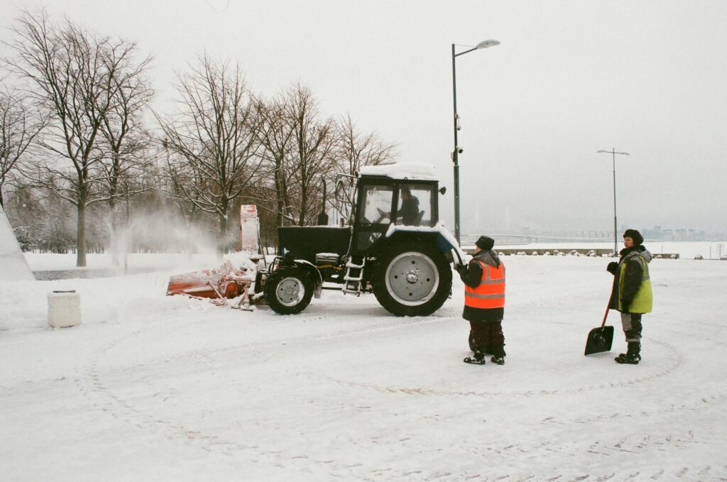 Workers using a tractor to clear snow on a winter street. Image of a snowy scene with road maintenance.